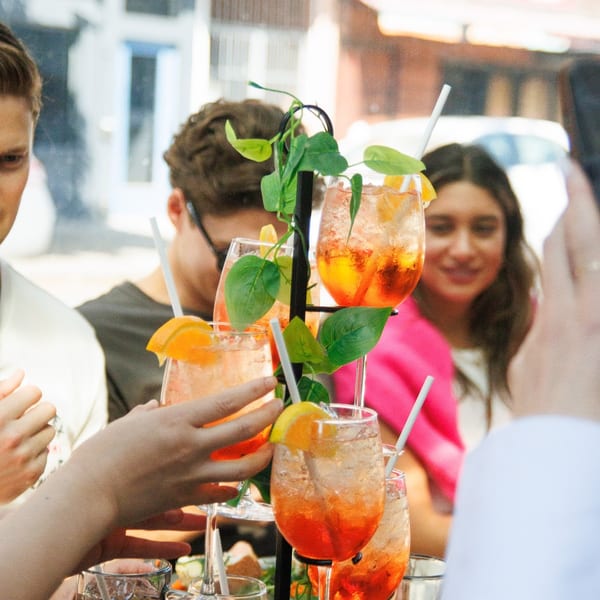 Friends enjoying orange cocktails with straws and orange slices at an outdoor restaurant.