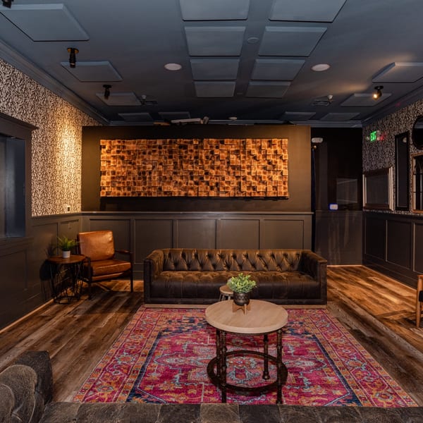 Dark, cozy lounge with leather seating, a fireplace screen, colorful rug, and wooden wall art.